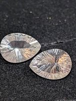 Two pear-shaped faceted white topaz gems on black background