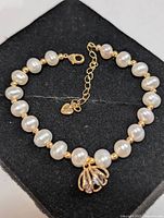 Bracelet on display box showing pearls, gold-tone beads, clasp, charm