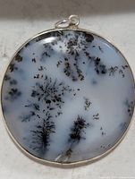 front view of round dendritic opal pendant showing inclusions and silver bezel