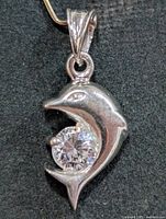 Front view of silver dolphin pendant holding CZ