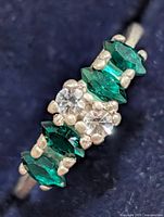Oblique view showing marquise green stones and round clear stones in prong setting