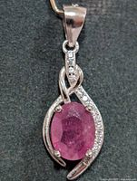 Front view of silver pendant with oval ruby CZ and clear CZ accents in twisted ribbon setting