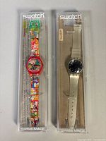 Both Swatch watches in their clear cases