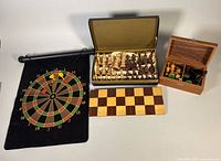 Group shot showing roll-up dart board with darts, lined case with chess pieces, second wood box with pieces, and folded chess board