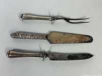 Three utensils laid out: carving fork, cake server, carving knife