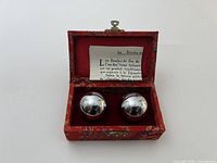 Open brocade case showing two chrome Baoding balls and instruction leaflet
