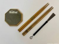 Front of Evans RealFeel practice pad alongside two pairs drumsticks and one brush