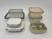 Group of seven rectangular food storage containers, various lid colors, one stainless body visible