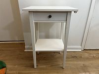 Front view of white IKEA Hemnes nightstand showing drawer, knob, shelf, and legs