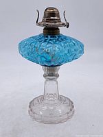 Full view of oil lamp showing aqua hobnail font, clear pressed glass base, and metal burner