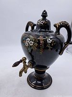 Full view of black ceramic samovar showing floral decoration, handles, lid and base