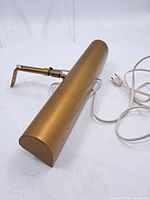Full view of gold/brass picture light with cord and adjustable bracket