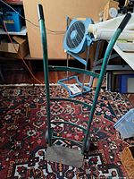 Full view of green hand truck standing upright on rug