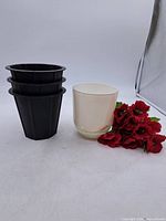 Group shot showing three black nursery pots stacked, white outer pot, red faux flowers
