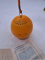 Full view of orange-shaped radio hanging by strap, showing speaker holes and overall texture