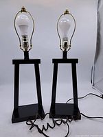 Front view of both black painted wood table lamps with bulbs and harps