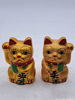 Front view of both gold Maneki-neko banks showing raised paws, painted details and kanji.