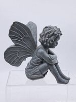 Left profile of seated fairy statue showing wings, dress and pose