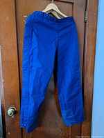 Full front view of blue rain pants on hanger