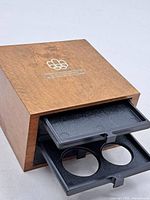 Closed wood coin box with one tray partially extended showing two coin recesses