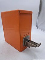 Full view of orange metal coin bank showing lever mechanism