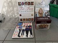Group shot of all five items: two cookbooks, Food Network magazine, Crock-Pot recipe card tin, clear plastic holder
