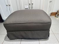 Front view of grey upholstered ottoman with skirt