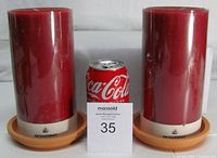 Front view of two sealed Bowring red pillar candles on terracotta saucers with scale reference