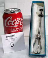 Tongs in box beside soda can showing scale