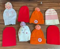 Overview of eight assorted knit beanies laid out on floor