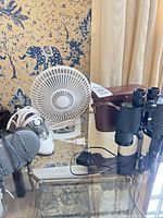 Binoculars in case, desk fan, travel iron, sleep machine visible on glass table