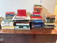 Overall view of three stacks of assorted books on wooden credenza