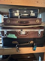 Stack of four cases showing KLM briefcase on top, two brown suitcases, black suitcase bottom