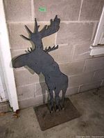 Full view of metal moose silhouette on stone base against concrete wall