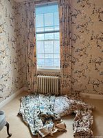 Window showing beige printed floral curtain pair, additional folded curtain sets on floor