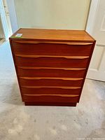 Front view of teak six-drawer dresser showing sculpted pulls and plinth base