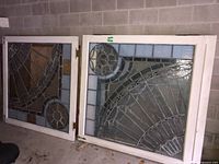 Two stained glass panels leaning against wall showing design and missing pieces