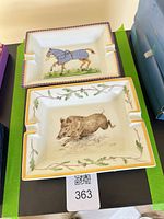 Two Hermès porcelain ashtrays stacked; top shows horse design, bottom shows boar design