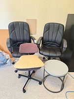 Group shot of two black office chairs, one fabric chair, and round side table