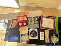 All boxed items arranged on table including fan, magnets, iron balls, bookmark, stopper, stained glass, plaque, quaich