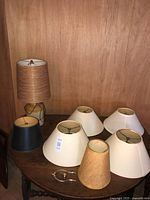 Table lamp with attached cylindrical shade and six extra conical shades on round table