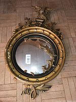 Front view of round convex mirror showing eagle crest, scroll decorations, broken pieces