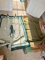 Overview of three wool blankets laid on floor, Ralph Lauren Polo blanket left, two green blankets stacked right