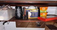 Shelf with extension cord in bin, bug zapper, two flashlights, loose SmartLight light, boxed SmartLight lights, two OFF! candle boxes, red fire blanket case