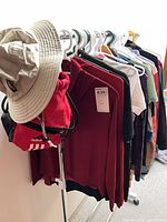 Rack with assorted women’s athletic tops, beige hat, red Adidas bag visible