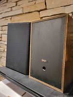 Front and rear of one speaker showing grille on and back panel with terminal and port