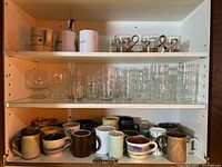Cabinet view showing mugs on lower shelf, glasses on middle shelf, decorative cups on upper shelf