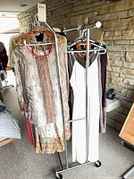 Full view of chrome metal clothing rack loaded with garments to show scale and two hanging rails