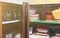 Cabinet shelves with glass jars, bowls, salad spinner parts, baking trays and cutting boards visible