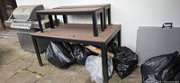 Large bench/table with two smaller pieces stacked on top next to grill and garbage bags